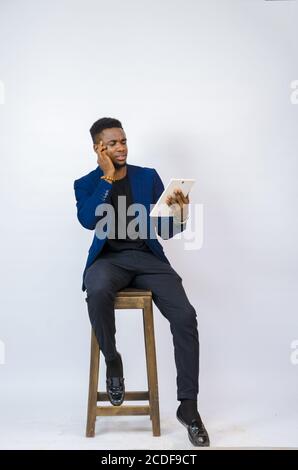 Young African male sitting on a chair and looking at his tablet Stock Photo