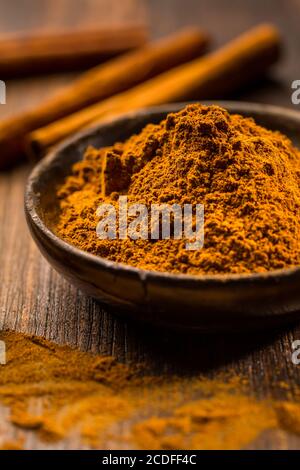 Cinnamon powder in wooden bowl with cinnamon sticks on wooden background as cooking and baking ingredient. Stock Photo