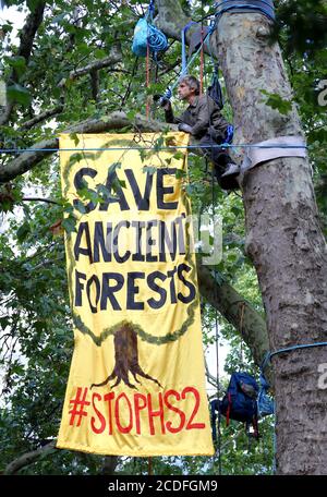 A Stop HS2 campaigner unfurls a banner in trees outside Euston Station in London as activists set up a camp within the trees as part of the wider Extinction Rebellion weekend of action across the country. Stock Photo