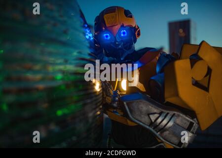 Robot transformer stands in street and glows in dark against background of night city. Stock Photo
