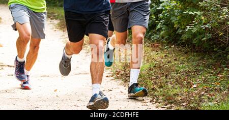 Front view of the legs of three high school boys running on a dirt path in a park. Stock Photo