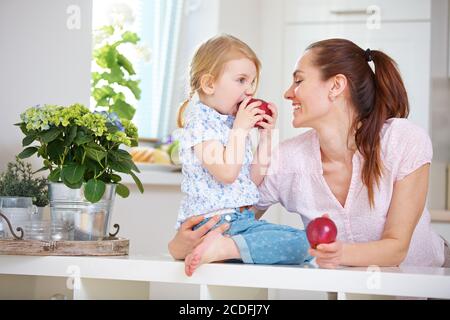 Mother and daughter each eat an apple in the kitchen Stock Photo