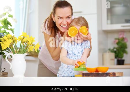 Mother holds oranges before daughter's eyes while squeezing juice in the kitchen Stock Photo