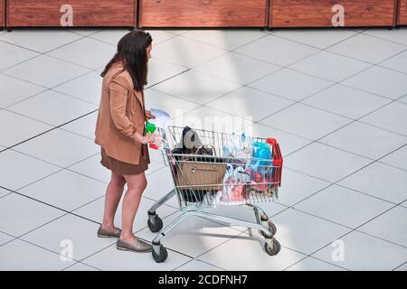 Voronezh, Russia, 23.08.2019 - Woman with shopping cart checks shopping list in market. Adult woman in supermarket pushing shopping trolley. Forgot to Stock Photo