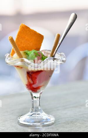 Close up of a delicious looking ice cream cup with crispy wafer sticks and a spoon on a table on an out of focus background. Sweet food concept. Stock Photo