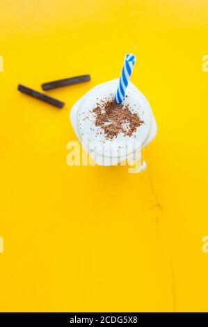 milkshake in glass mug witha handle and blue straw, sprinkled with chocolate on bright yellow background, minimalistic style Stock Photo
