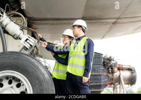 Asian man and woman engineer maintenance airplane team repairs, fixes, modernization and renovation in front airplane from  in airport. Stock Photo