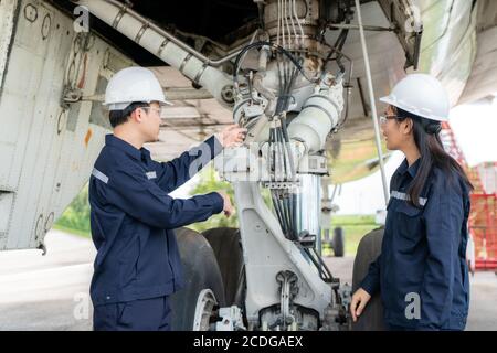 Asian man and woman engineer maintenance airplane team repairs, fixes, modernization and renovation in front airplane from  in airport. Stock Photo