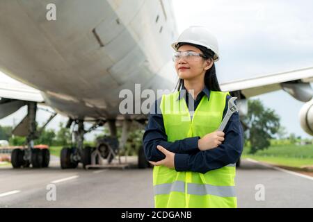Asian woman engineer maintenance airplane arm crossed and holding wrench in front airplane from repairs, fixes, modernization and renovation in airpor Stock Photo