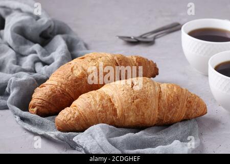 Two fresh croissants and two cups of coffee on a light grey concrete background. Breakfast or lunch concept. Closeup Stock Photo