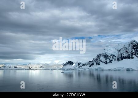 Mountain range in Antarctica covered in snow and ice with icebergs floating in the ocean. Stock Photo