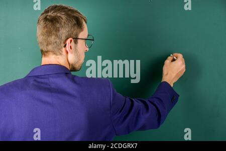 Teacher write on chalkboard rear view, explaining to students concept. Stock Photo