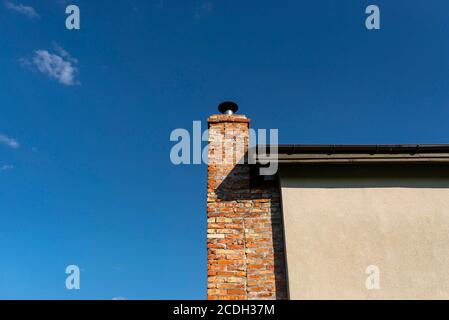 A red ceramic brick chimney standing at the rear of the building, by the facade, with a blue sky in the background. Stock Photo
