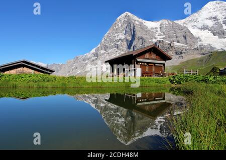 A swiss mountain chalet reflecting in a calm pond with the iconinc north face of Eiger Mountain in the Bernese Alps, Switzerland. Stock Photo