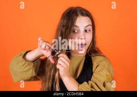 Cute girl cutting hair to herself with scissors. kid is trimmed in the hairdressers. child with scissors wants to cut hair. girl in hairdressing salon. teenager cutting hair. Do expect greatness. Stock Photo