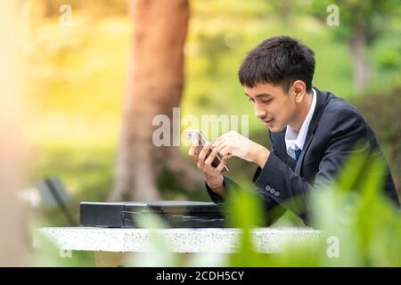 A handsome young asian business man using smartphone. A happy businessman sitting on a table. Stock Photo