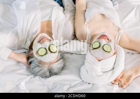 Close up top image of women, senior gray haired lady mother and her young pretty daughter having fun in the bedroom and making clay facial masks with Stock Photo