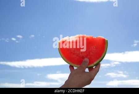 Hand holds a slice of watermelon on a blue sky background Stock Photo
