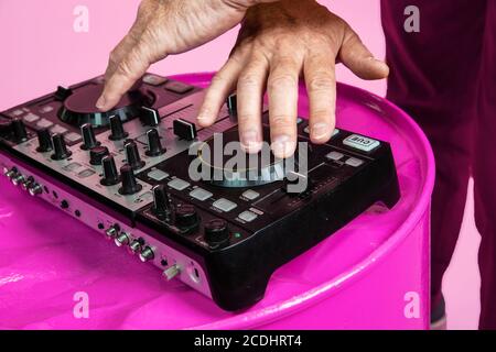 Party drive. Close up senior man playing DJ set isolated on pink studio background. Tech and joyful elderly lifestyle, music, festival concept. Trendy colors, forever youth. Copyspace for your ad. Stock Photo