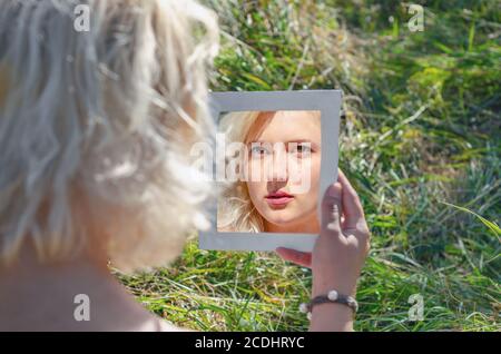 Blonde woman looking in the mirror on nature. View from behind. Stock Photo