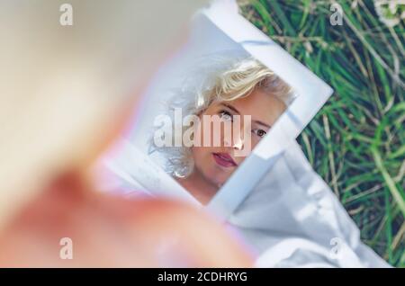 Blonde woman looking in the mirror on nature. View from behind. Stock Photo