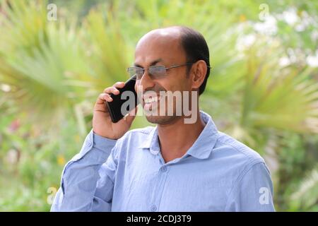 Smiling Asian man talking on mobile phone outside in a park Stock Photo
