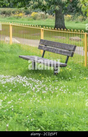 Overgrown solitary public seat / bench in a kid's playground empty of people during UK Covid lockdown. Deserted public space, empty park bench in UK. Stock Photo