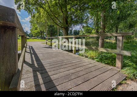 Small wooden footbridge over the Keutelbeek stream with lush green trees on the shore seen from a bottom perspective, sunny summer day in Sittard in S Stock Photo