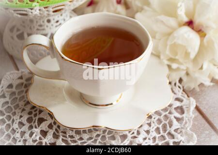 Tea on a summer day. Still life with a cup of tea, white bouquet of peonies on a white lace tablecloth Stock Photo