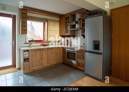 Corner kitchen with window in small apartment. Wooden furniture in warm tones, wide angle view. Stock Photo