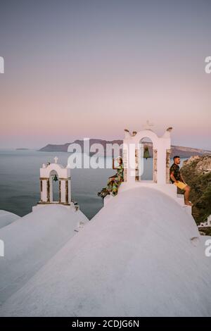 Santorini Greece, young couple on luxury vacation at the Island of Santorini watching sunrise by the blue dome church and whitewashed village of Oia Stock Photo