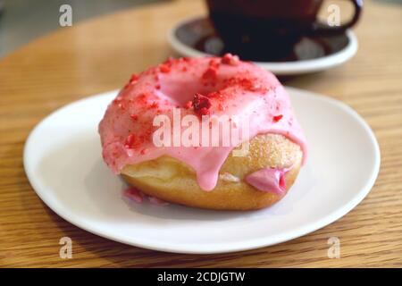 Mouthwatering strawberry-glazed with raspberry cream filling doughnut on a white plate Stock Photo