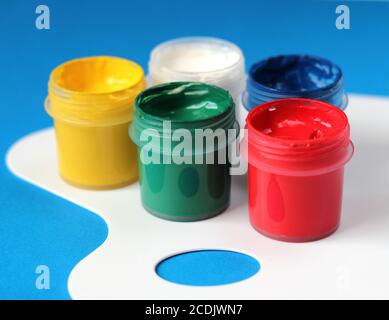 Containers of bright watercolor paints and white paintbrushes palette on blue background. Stock Photo