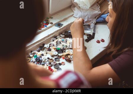 Mother and daughter are sitting at home doing needlework from buttons and fabrics while staying at home in quarantine. Stock Photo