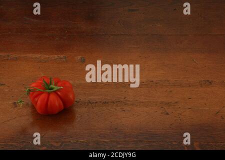 Close up of one ripe heirloom tomato seen on the dark surface of an oak table as background. Stock Photo