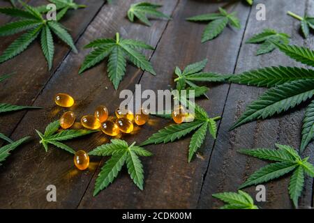 CBD oil capsules and green cannabis leaves on rustic wooden table Stock Photo
