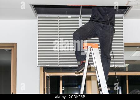 The mechanic is cleaning the air conditioner in the office. Worker repairing ceiling air conditioning unit. Stock Photo
