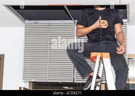 The mechanic is cleaning the air conditioner in the office. Worker repairing ceiling air conditioning unit. Stock Photo