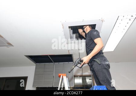 The mechanic is cleaning the air conditioner in the office. Worker repairing ceiling air conditioning unit. Stock Photo