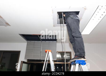 The mechanic is cleaning the air conditioner in the office. Worker repairing ceiling air conditioning unit. Stock Photo