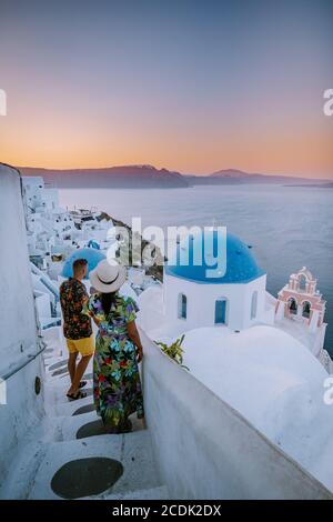 Santorini Greece, young couple on luxury vacation at the Island of Santorini watching sunrise by the blue dome church and whitewashed village of Oia Stock Photo