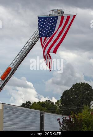 A large American flag waves in the breeze as it hangs from the ladder of a fire engine outside of President Trump's speech in Mills River, NC Stock Photo