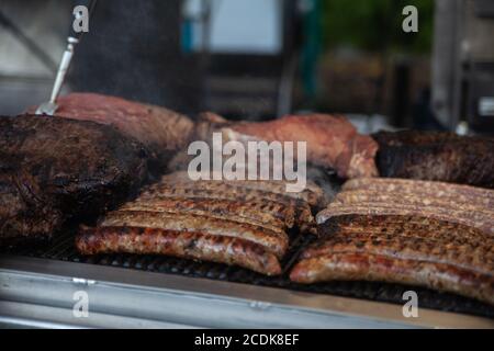 Italian sausages and smoked brisket are cooking on the food stand grill during a country fair. Stock Photo