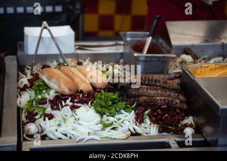 Italian sausages, onions, bell peppers, and hot dog buns are on the food stand during a country fair. Stock Photo