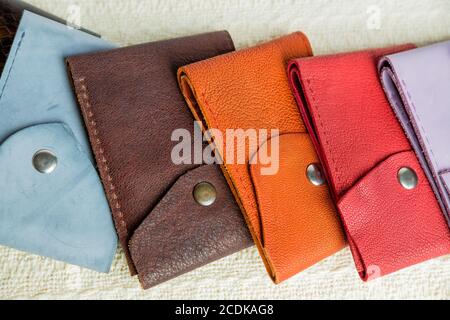 Colorful leather wallets.Leather handmade wallets of different forms lying on a beige textile background. Selling point leather goods. Stock Photo