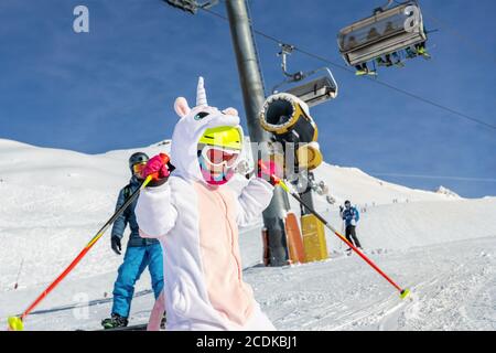 Cute adorable preschooler caucasian kid girl portrait with ski in helmet, goggles and unicorn fun costume enjoy winter sport activities. Little child Stock Photo