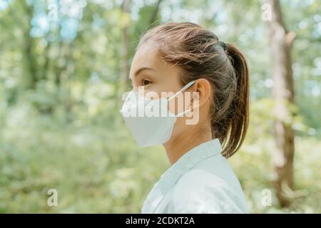 Asian woman wearing face mask walking in outdoor nature. Eco-friendly sustainable masks concept. Woman with korean kn95 mouth covering for corona Stock Photo