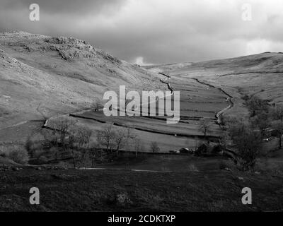 Black & white view of farmhouse at Gordale Beck & fields beside Hawthorns Lane winding up to the high fells above Malham North Yorkshire, England, UK Stock Photo