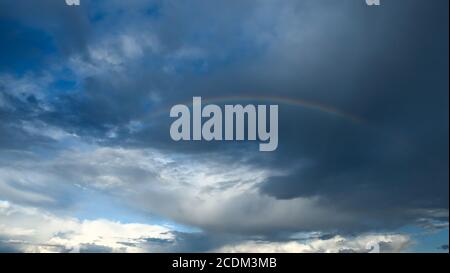 Amazing dramatic sky. Cloudy weather turning rainy. Cumulonimbus in atmosphere with rainbow. Stock Photo