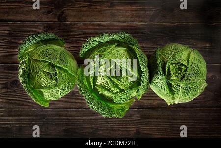 Three savoy cale cabbage heads on dark wooden board, view from above Stock Photo
